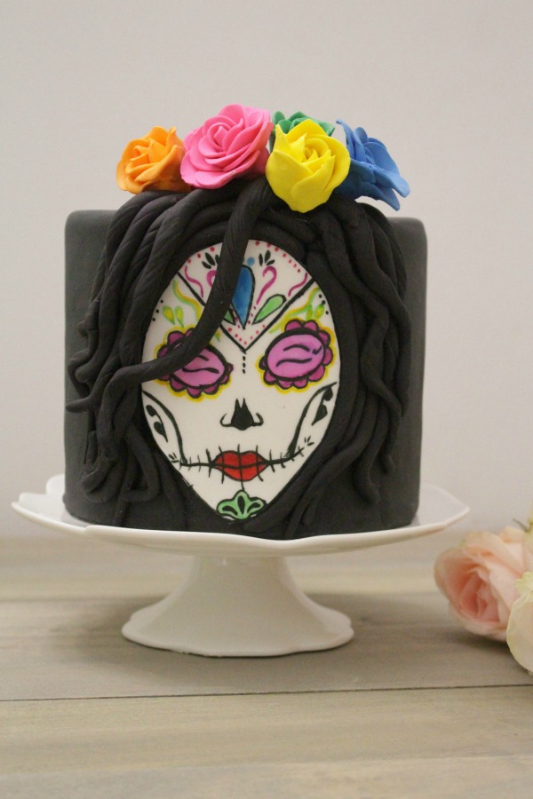 Behind the cake-Cake covered in black fondant with a sugar skull face painted in watercolors with sugar flowers