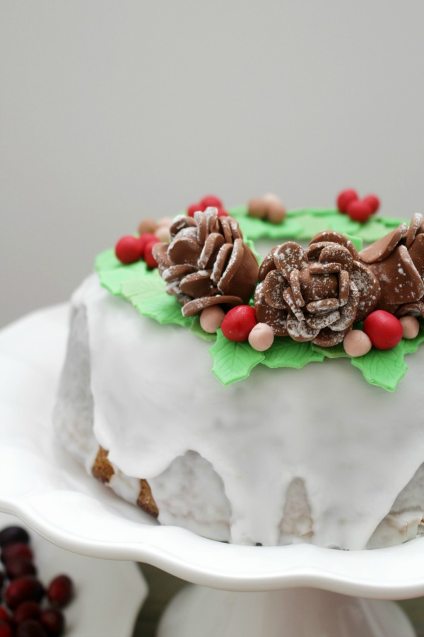 Behind the cake - Christmas bundt cake decorated with green mistletoe leafs made out of fondant, pine cones and berries.