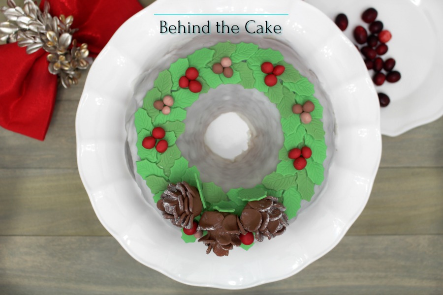 Behind the cake - Christmas bundt cake decorated with green mistletoe leafs made out of fondant, pine cones and berries.